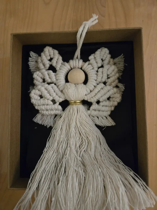 A handmade macramé angel resting in a gift box