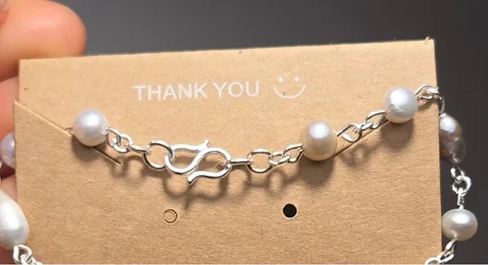A pearl bracelet on a kraft card printed with the words Thank You